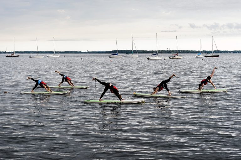 A group of women maintain balance during an Outdoor UW standup paddleboard (SUP) yoga class